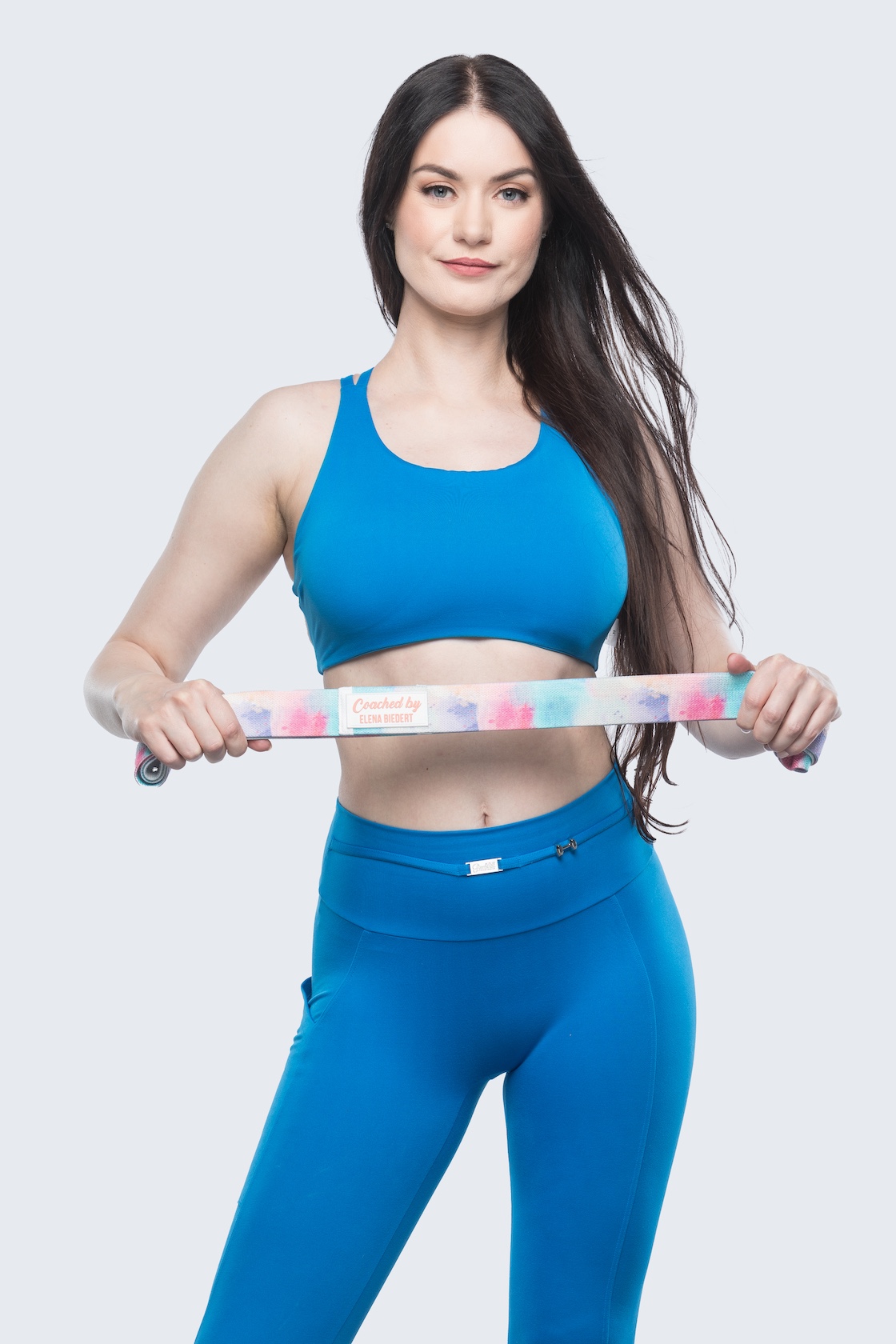 Elena wearing a blue sports bra and legging set, holding her resistance workout band in front